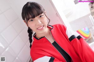 A woman sitting on top of a bed wearing a red jacket.