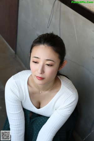 A woman in a white bra and green skirt standing by a window.